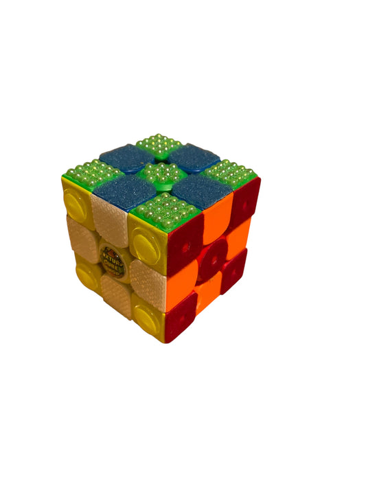 Texture Cube pictured in checkerboard pattern to show off six distinct sides. Orange side: smooth plastic. Yellow side: large, round piece on each square. Red side: soft velvet with a punched hole in the centers. White side: Grippy texture. Blue side: Fluffy, carpet-like. Green side: Bumpy texture made of pearls.